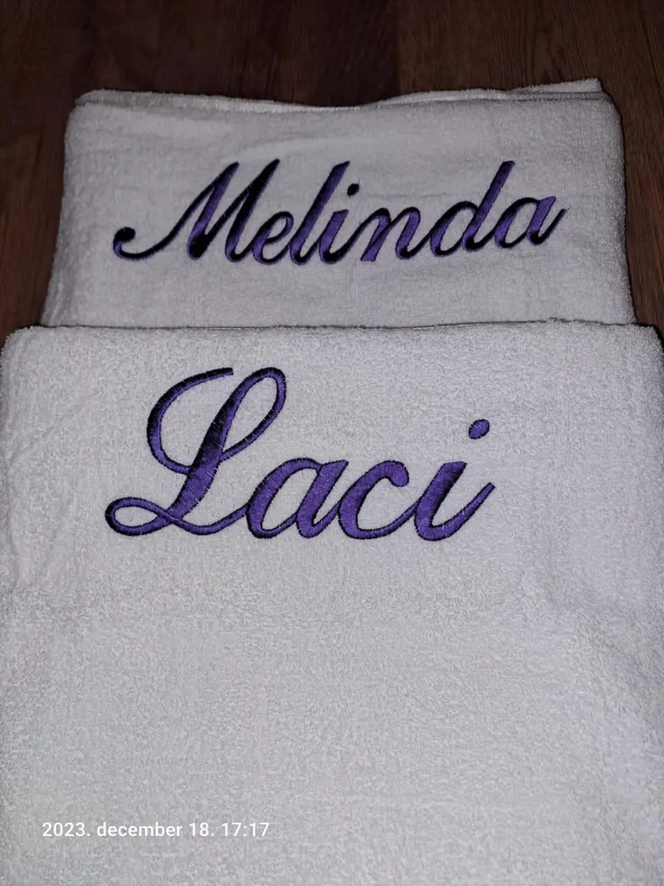 „Melinda” és „Laci” név lila hímzéssel fehér törölközőkön